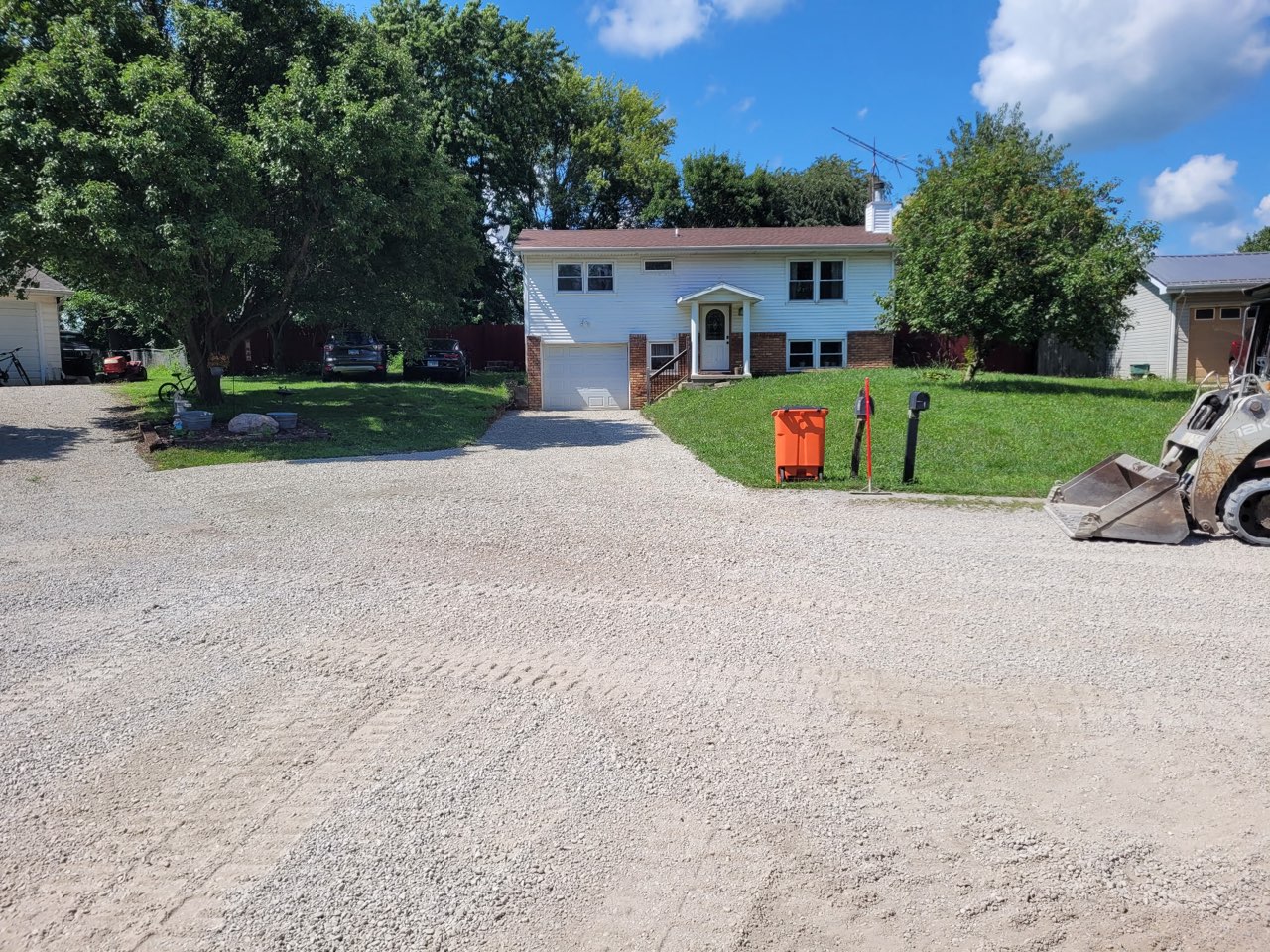 Freshly placed and compacted rock parking pad and driveway apron in Mattoon, Illinois, with the skid steer still on site — Brohez Trucking LLC