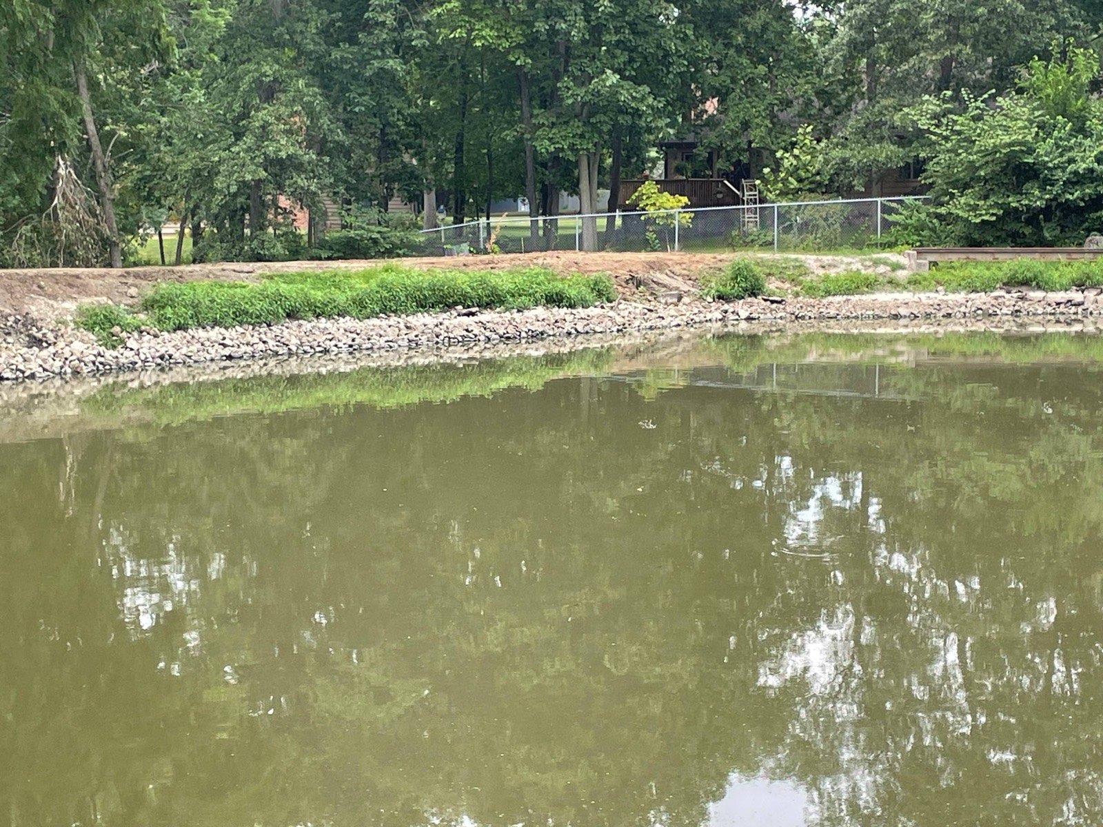 Rebuilt pond dam with a fresh riprap-armored bank and the pond refilling, after a 40-foot dam repair near Decatur, Illinois — Brohez Trucking LLC